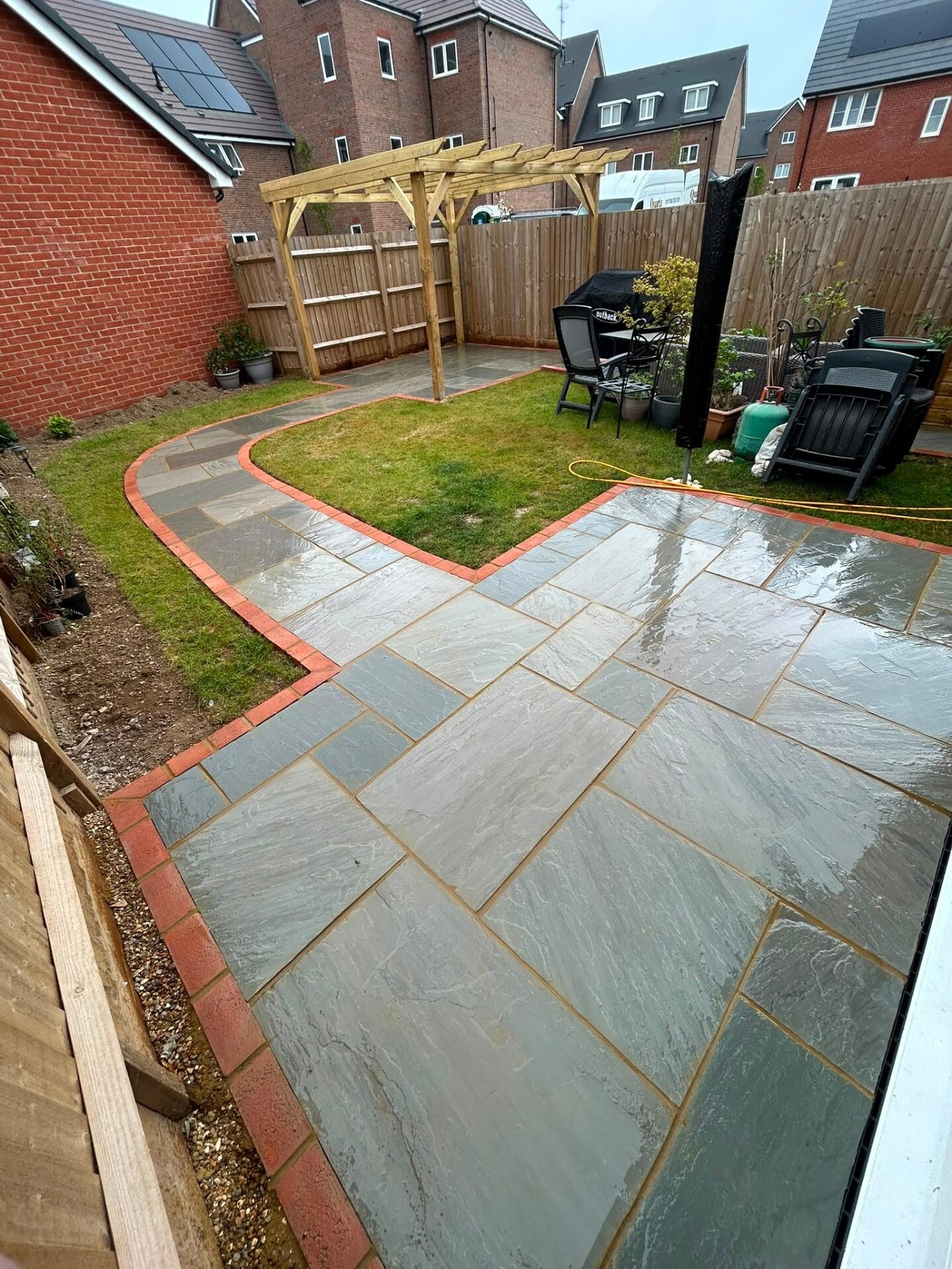Timber pergola over a sandstone patio with red-brick edging and lawn.