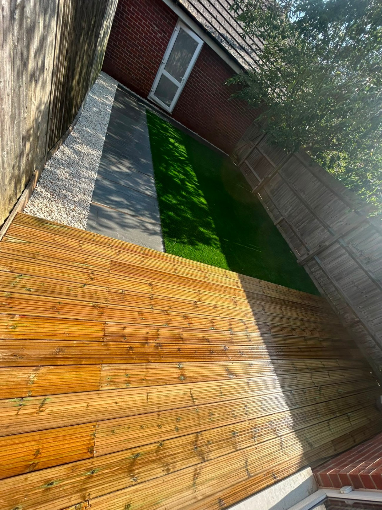 Timber deck, artificial lawn, paving slab path and gravel border in a low-maintenance Sussex back garden.
