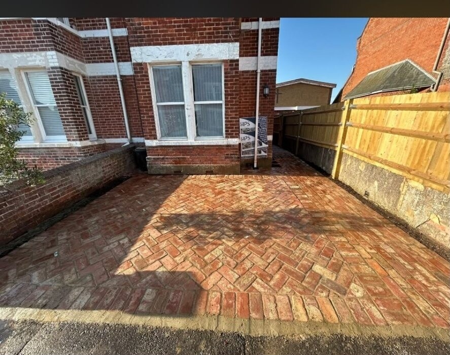 Red clay-brick path running tightly along the side wall of a Sussex home.
