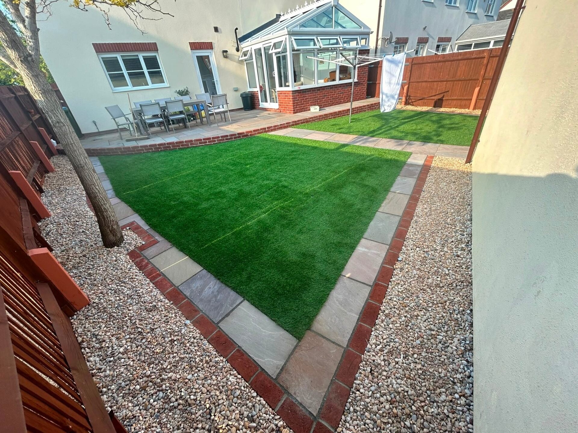 Premium artificial grass lawn framed by a red-brick mowing strip — recent install by Heavens Property Solutions.