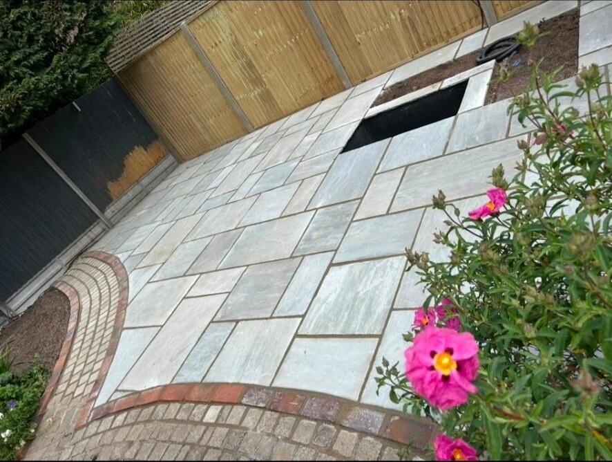 Sandstone patio with red-brick edging and a planted border.