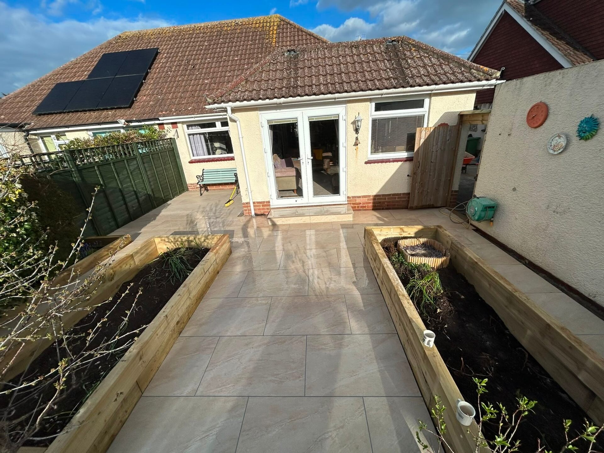 Sandstone patio and timber raised planters at the rear of a solar-panelled bungalow.